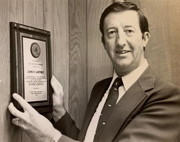 Jack Gaffney stands with his plaque on the wall in his office